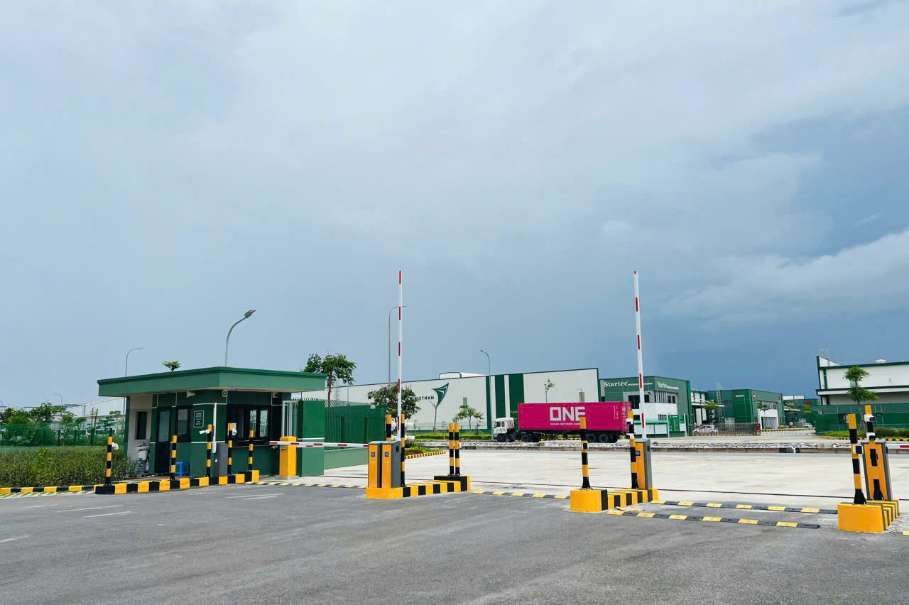 Cổng bảo vệ khu công nghiệp hiện đại với barie tự động và xe container màu hồng ONE bên trong